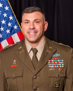 A picture of a white male in US Army dress attire with the American flag behind him.
