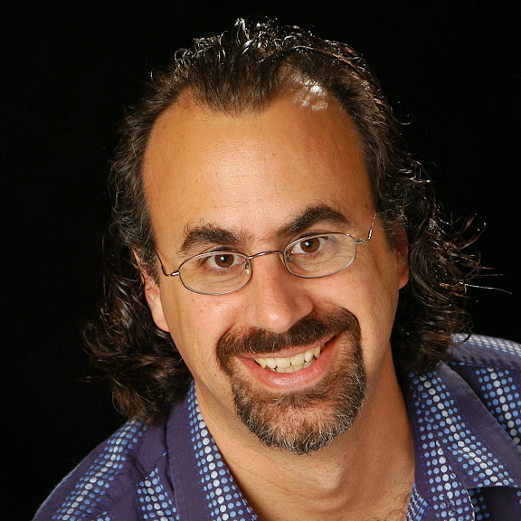 A headshot of Dr. Stephen M. Fiore. A white male with dark brown hair and glasses wearing a blue striped shirt and smiling into the camera.