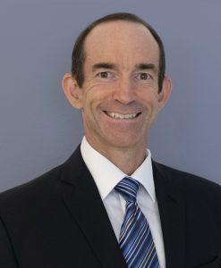 White male smiling against a light blue backdrop.