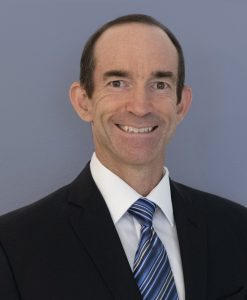 Scott Dillon White male smiling against a light blue backdrop.