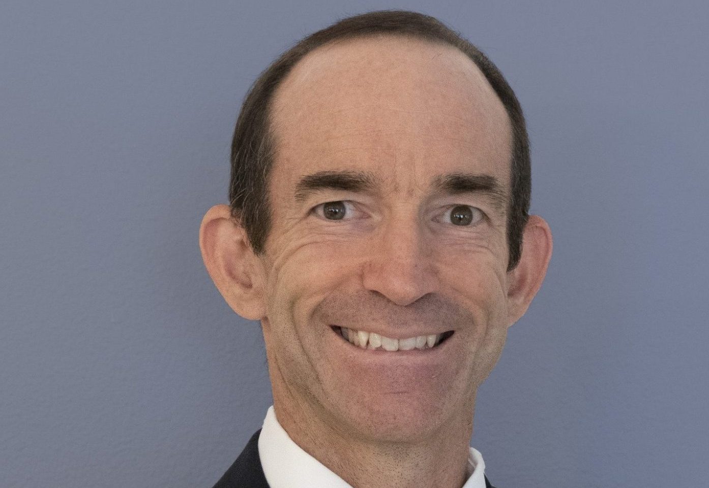 White male smiling against a light blue backdrop.