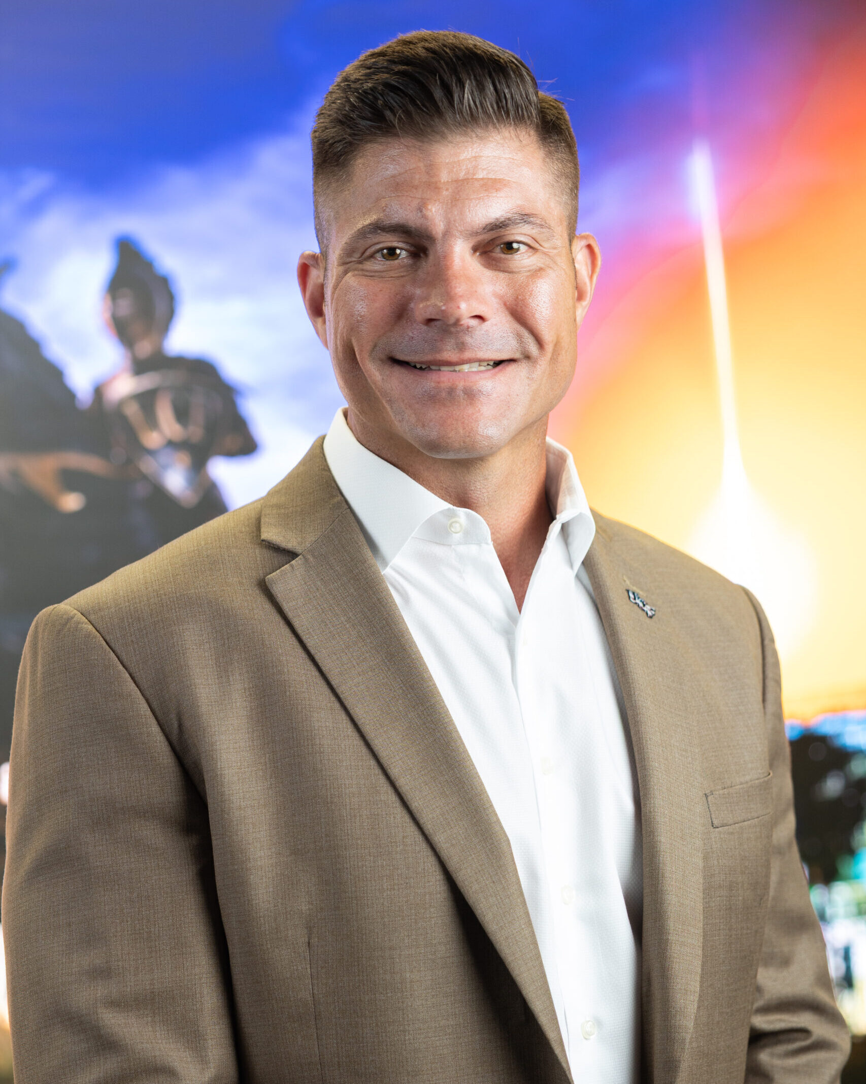 White man in a brown suit standing in front of a background with a knight on a horse and a space ship ascending into the sky.